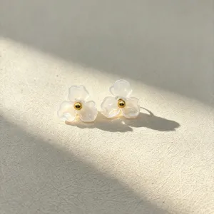 Close-up detail shot of white resin flower stud earrings with a gold center bead, elegant.