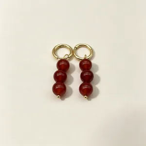 Detailed shot of gold-plated hoop earrings featuring three dangling red agate round beads for women.