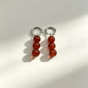 Close-up detail of elegant red stone bead hoop earrings with polished metal rings.