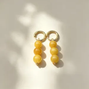 Close-up detail of golden hoop earrings featuring yellow stone beads hanging in soft natural light.