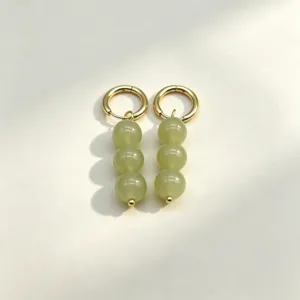 Detailed close-up view of elegant gold hoop earrings featuring hanging green round drops.