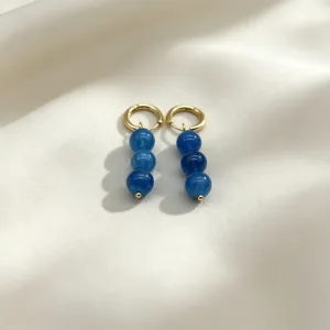 Detailed shot of golden hoop earrings featuring blue round bead drops on elegant silk fabric