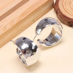 Closeup of trendy chunky silver metal hoop earrings with hammered texture for stylish women.