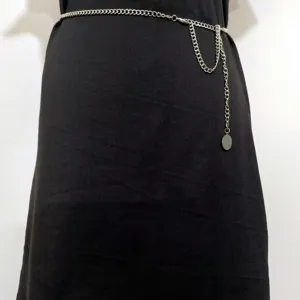 Detail shot of a vintage silver metal waist chain with a hanging round pendant on black dress.