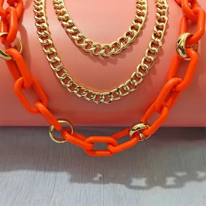 Detailed shot of layered chunky chains featuring bright orange resin and shiny gold links.