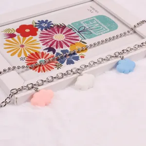 Close-up detail of double layer metal chain with colorful cloud charms on white plush background.