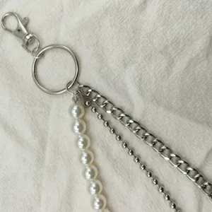 Detail shot of a trendy multi-layer pants chain featuring faux pearls and metal chains.
