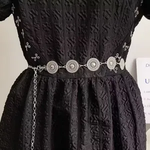 Detailed shot of a stylish silver metal waist chain with intricate disc patterns on dress.