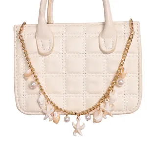Gros plan detail de sac a main beige matelasse avec chaine breloque coquillage et perle.
