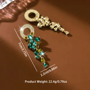 Primo piano di lussuosi orecchini pendenti a foglia dorata con strass di cristallo verde scintillante.