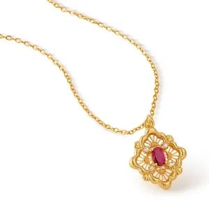 Gros plan sur le collier pendentif floral filigrane plaque or avec une pierre rouge.