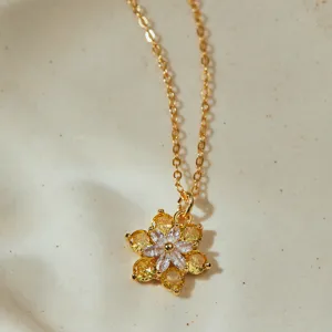 Primer plano de un collar chapado en oro con colgante de flor en circonitas amarillas y blancas.