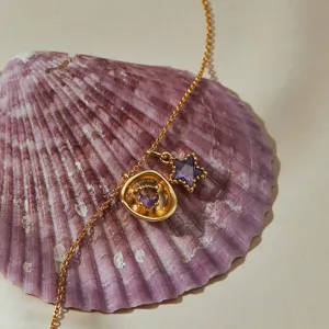 Close-up detail of a gold chain necklace with purple zircon star and round pendants.