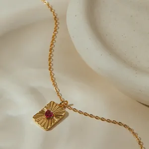 Délicat collier ras de cou plaqué or 18K avec pendentif cœur rubis et motif solaire.