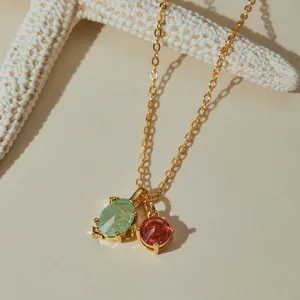 Detail shot of a gold-plated O-chain necklace featuring dual green and red stone pendants.