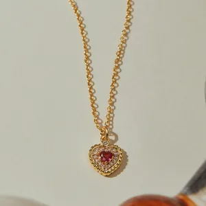 Gros plan d'un collier pendentif cœur plaqué or avec des pierres zircones rouges.