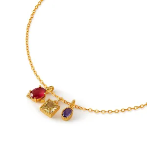 Close-up detail of a gold-plated necklace featuring three colorful cubic zirconia charms.