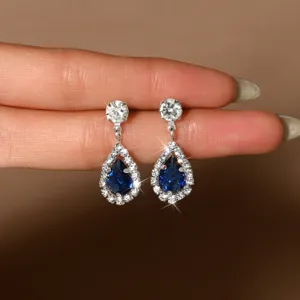 Primer plano detallado de elegantes pendientes de zircón azul con lágrima y halo brillante.