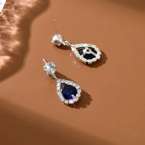 Primer plano detallado de pendientes de botón de plata con circonita azul y halo de cristales.