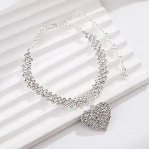 Detail shot of sparkling rhinestone chain and heart pendant on white textured background.