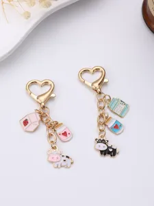 Detailed closeup of cute cartoon cow and milk bottle metal keychains with heart clasps.