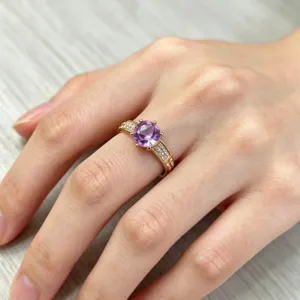 Nahaufnahme Detail des goldenen Luxusrings mit lila Rundstein und funkelnden Zirkonia Steinen.