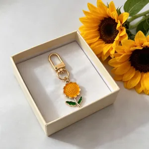 Detailed view of a cute enamel sunflower keychain pendant in a gift box with floral prop.