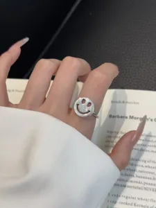 Primer plano de anillo de plata con cara sonriente en el dedo, diseño abierto y elegante.