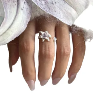 Minimalistischer silberner offener Ring mit zarter lilafarbener Lilienblüte und Herzanhänger.