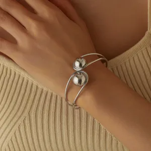 Dettaglio elegante del bracciale rigido aperto con doppia sfera argentata e superficie liscia.