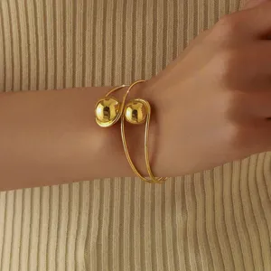 Primo piano dettagliato di un elegante bracciale rigido dorato con due sfere lisce.