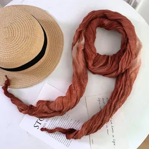 Detail shot of a stylish gradient tie-dye scarf on a white table with straw hat prop.
