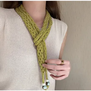 Detail shot of a green knitted hollow skinny scarf with beaded ends worn by a model.