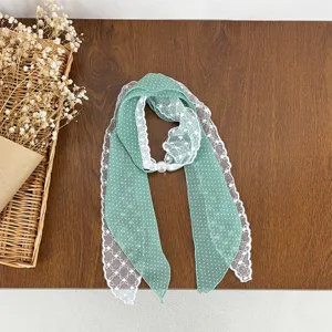 Detailed view of green polka dot scarf with delicate white lace trim and pearl buckle accessory.