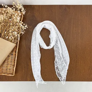 Close-up detail of white lace floral scarf with elegant pearl buckle on textured wooden table.
