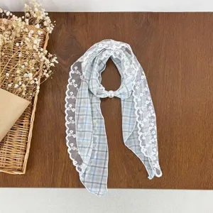 Close-up detail of blue plaid lace scarf with elegant white lace trim and pearl buckle.