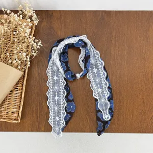 Detailed shot of a stylish blue patterned silk scarf featuring delicate white lace trim and a pearl accent.