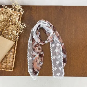 Detail view of brown printed lace patchwork silk scarf with elegant pearl accent for women.