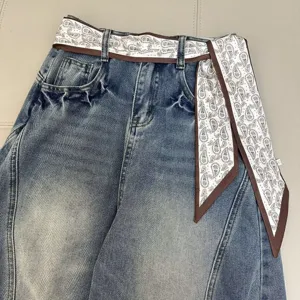 Detail shot of retro washed blue jeans featuring brown paisley print ribbon belt decoration.