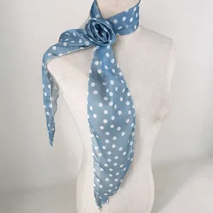 Détail en gros plan d'un foulard en mousseline à pois bleus avec une rose 3D amovible.