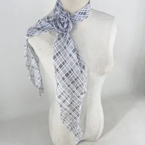 Gros plan détail du foulard en mousseline à carreaux gris avec une fleur rose 3D amovible.