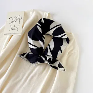 Close-up detail view of a chic black and white abstract print square scarf styled on knitwear.