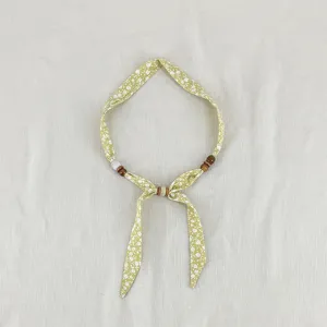 Close-up detail of green floral fabric scarf necklace with delicate wooden beads decoration.