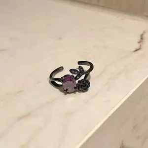Primer plano detallado de un anillo punk abierto chapado en negro con piedra morada y rosa.