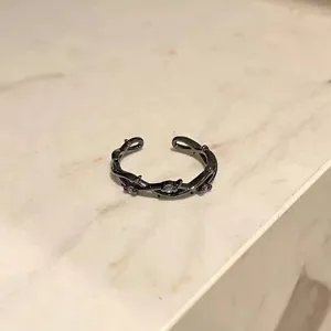 Vista detallada de un anillo abierto negro con diseño de espinas y cristales morados.