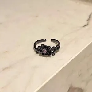Primer plano de detalle de anillo de rosa negra con cristal morado, estilo gótico punk.
