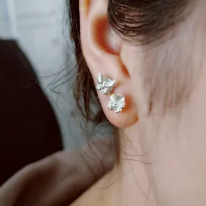 Close-up detail shot of dainty silver butterfly and flower stud earrings worn on earlobe.