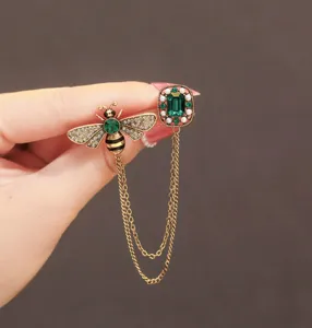 Vintage crystal bee and emerald rhinestone brooch with double chain detail for elegant outfits.