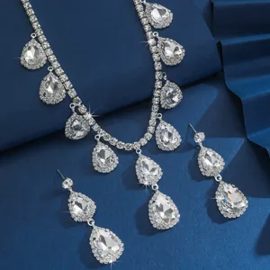 Dettaglio di set di collana e orecchini con strass a goccia scintillanti su sfondo blu.