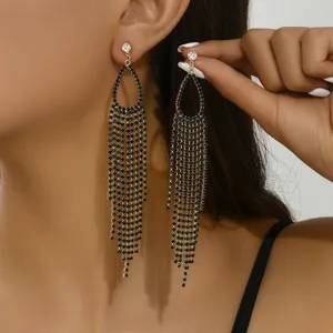 Primo piano dettagliato di lunghi orecchini con nappina in strass nero e pietre luminose.